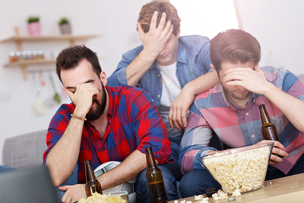 Sad male group of friends watching sports on TV at home