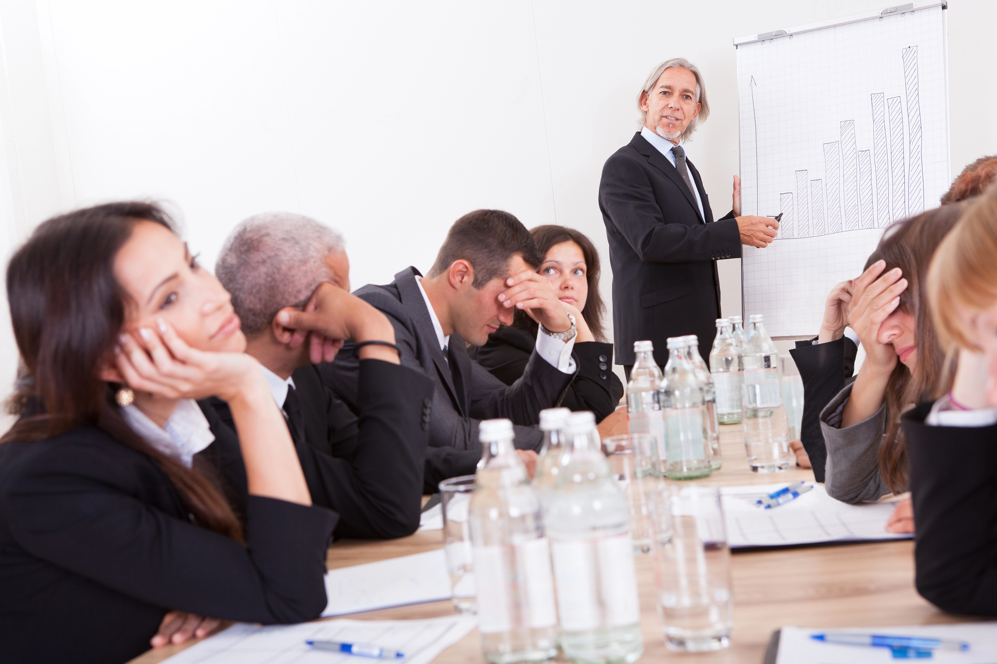 A visibly bored team in a meeting with the leader smiling and presenting obliviously