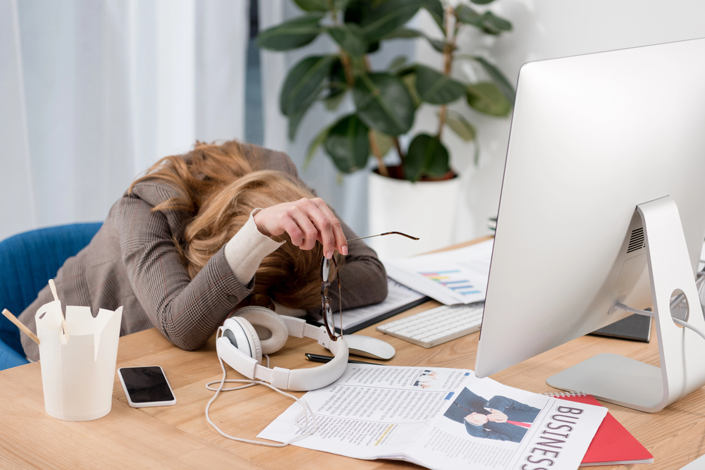 An exhausted businessworman banging her head on the desk