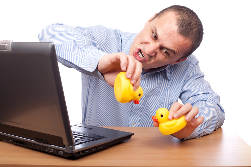 Businessmant at a desk with a laptop on it, playing with two rubber ducks