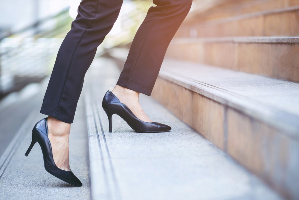 Women's feet in high heels climbing concrete steps with the sun setting in the background