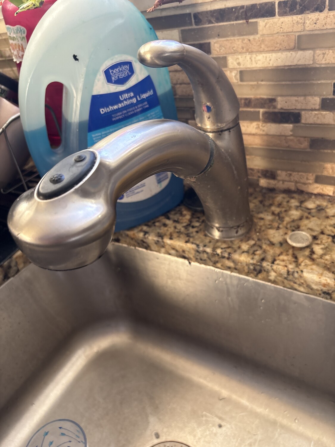 Close-up photo of a brushed stainless kitchen faucet set into a granite countertop over a brushed stainless basin